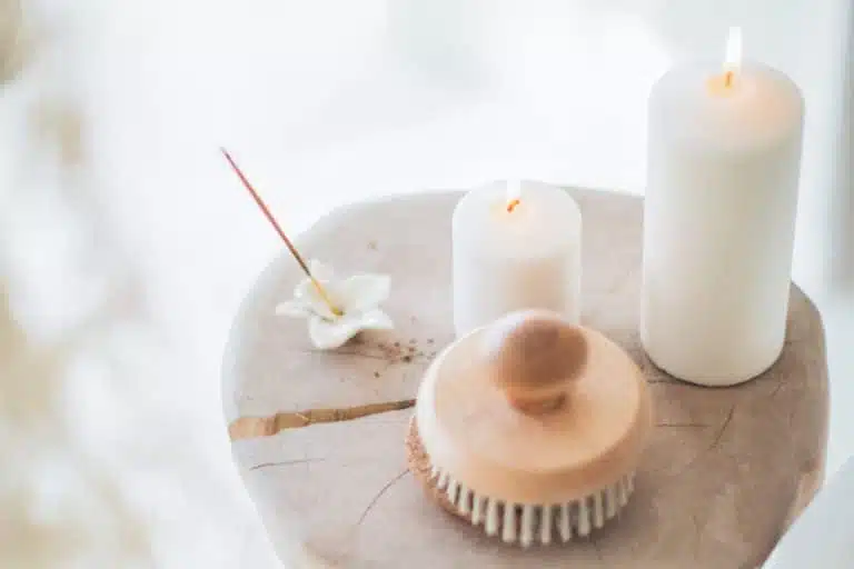 Several candles and a brush are arranged on a small birch log. The soft glow of the candles casts a warm and inviting ambiance, creating a serene atmosphere.