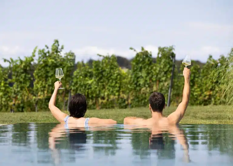 Couple with wine glasses in the pool and view of the vines