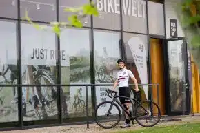 Viki Schnaderbeck im Fahrrad-Dress steht mit einem Fahrrad vor der LOISIUM BikeWelt.